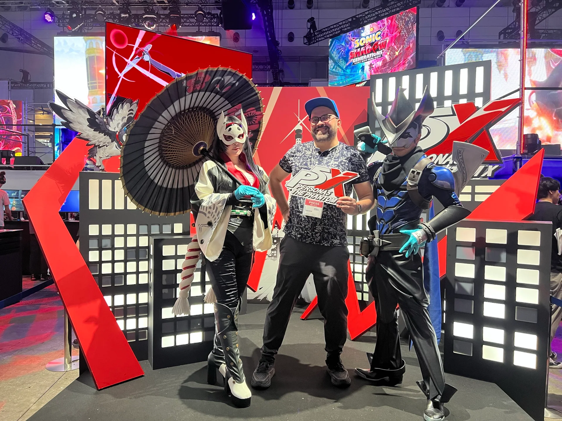 Michał Mazur przy stoisku Persona 5 na Tokyo Game Show, z identyfikatorem prasowym.